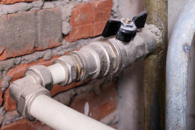 Close-up of a water shut-off valve against exposed brick wall.