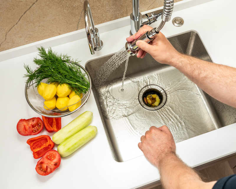 Person cleaning sink with vegetables nearby