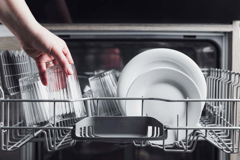 Hand loading dishwasher with dishes.