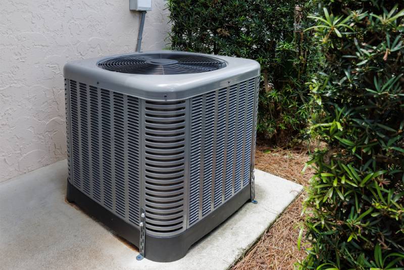 Outdoor AC unit on concrete slab near bushes.