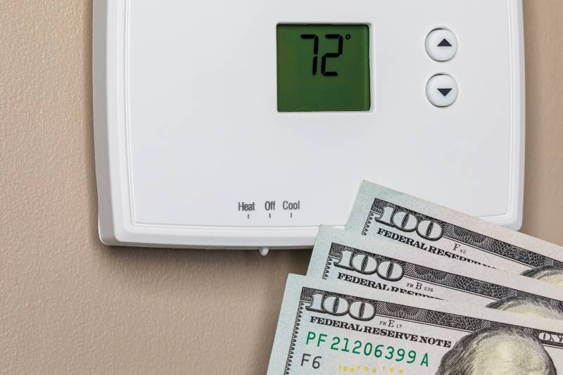 Thermostat showing 72°F with $100 bills underneath.