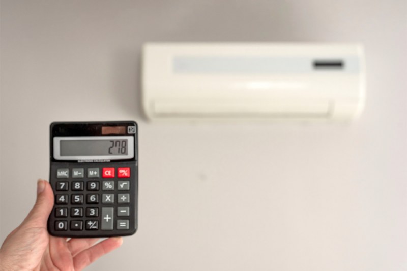 Hand holding calculator near wall-mounted AC unit.