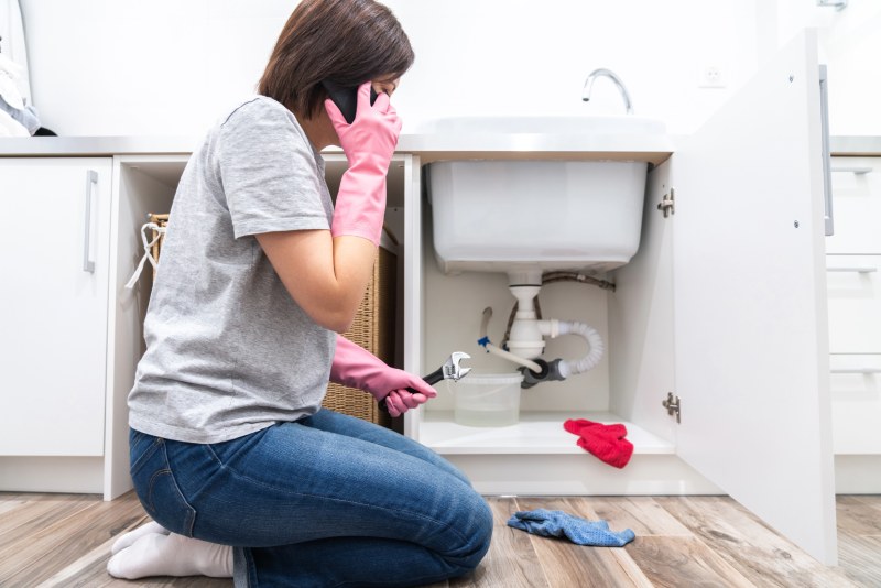 Woman on phone fixing leaking sink