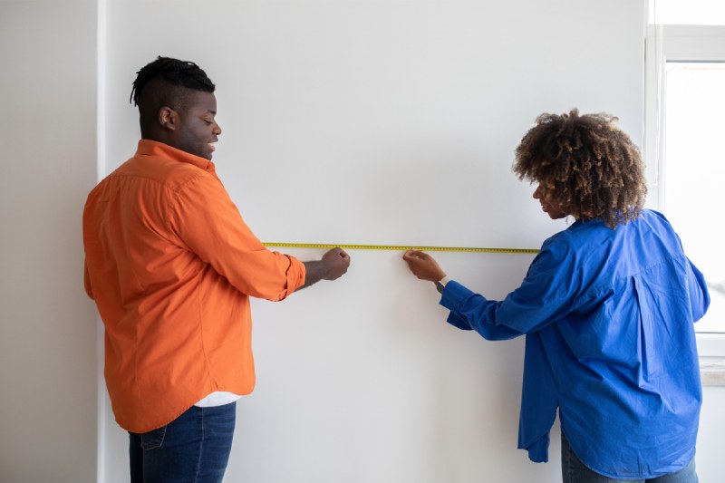 Two people measuring wall with tape measure.