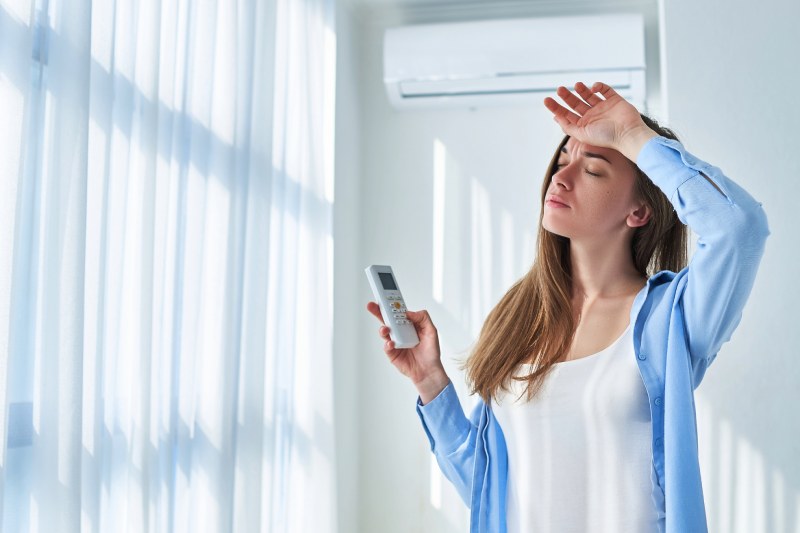 Woman sweating, holding AC remote.