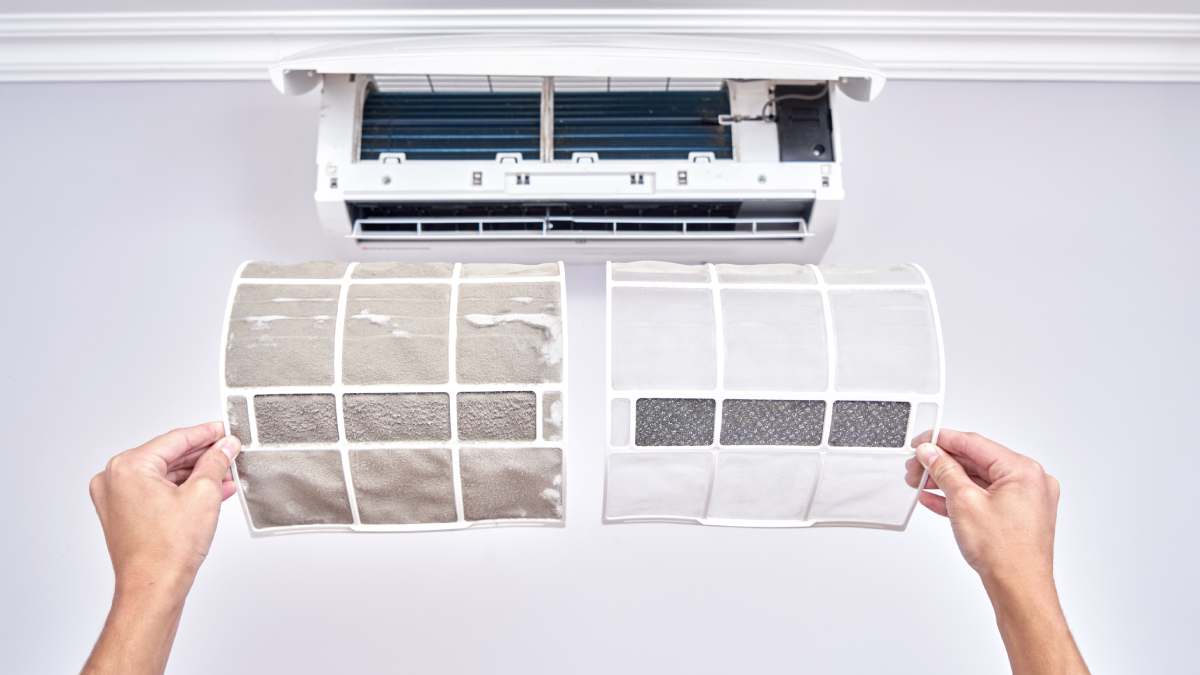 Two air filters, dirty and clean, held in front of an AC unit.