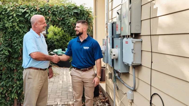 Technician and homeowner shaking hands near electrical panel.