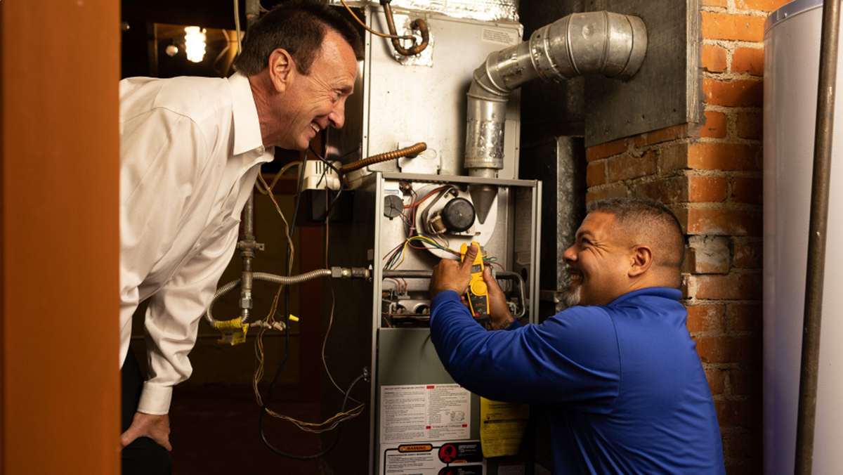 Technicians repairing a furnace in a basement.