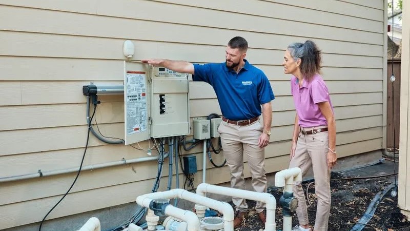 Electrician explains circuit panel to homeowner outdoors.