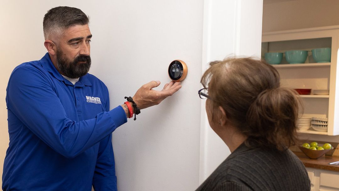 Technician demonstrates smart thermostat to homeowner.