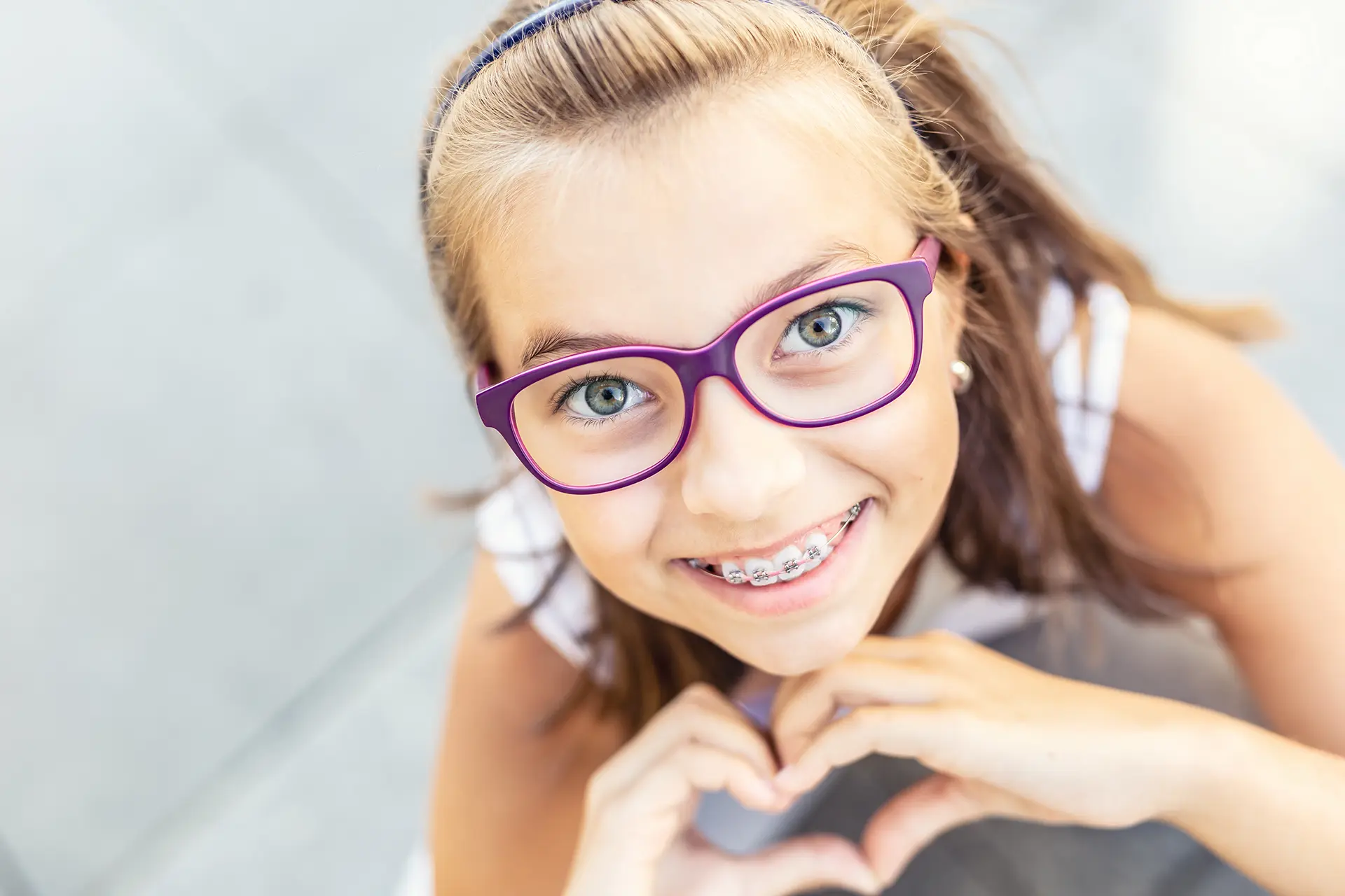 Girl with braces and purple glasses making a heart with her hands