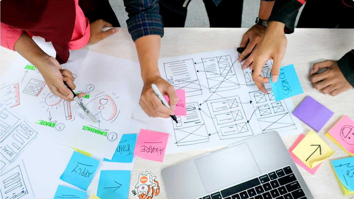 The hands of people on a desk working on a user experience project by using post it notes.