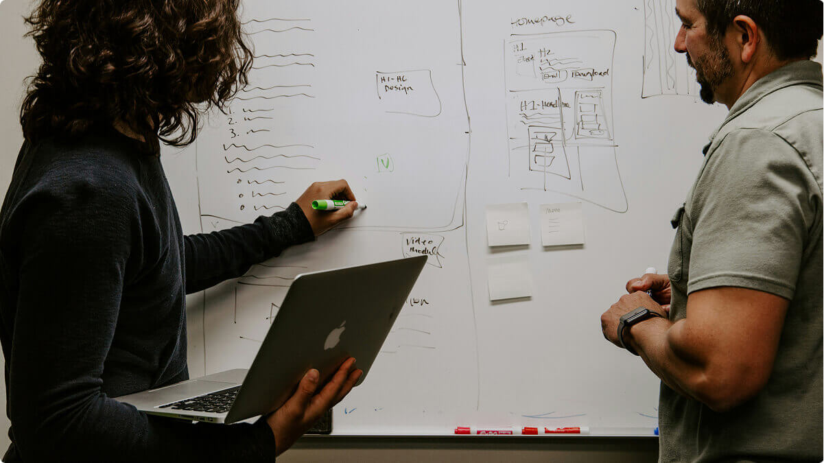 Two people collaborating on a piece of development work on a whiteboard.