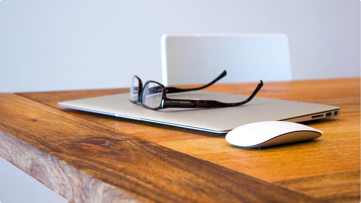 A desk with a laptop on it and a pair of glasses on top of the laptop.