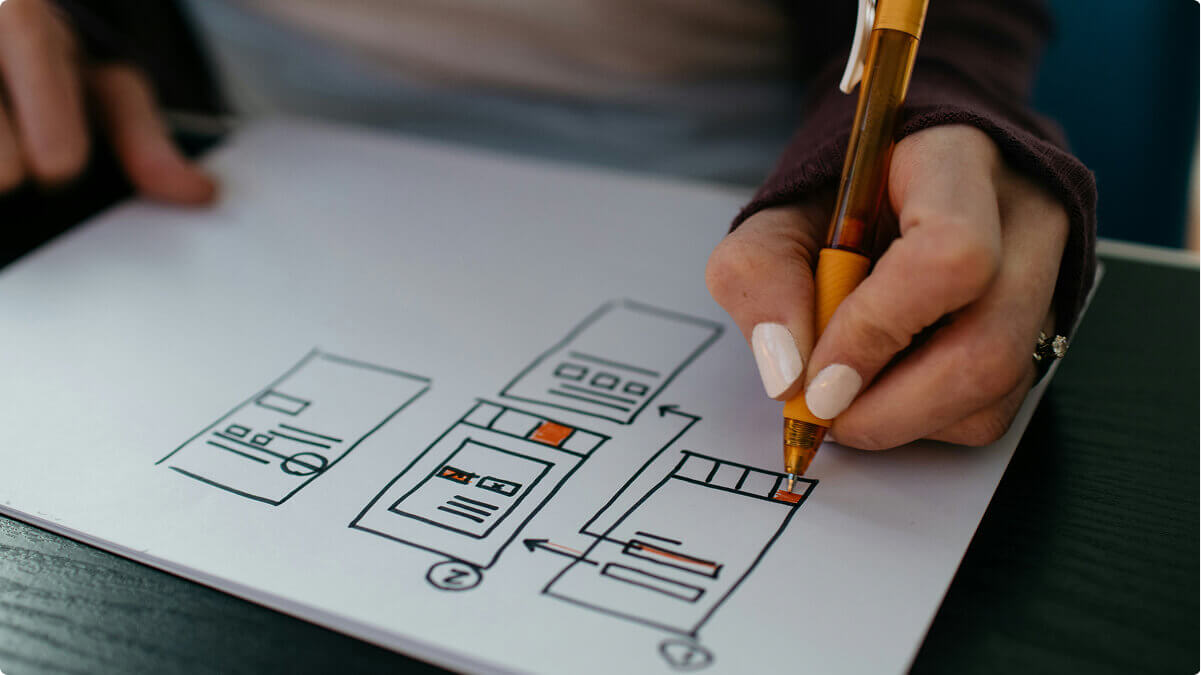 The hands of someone writing a UX design process on a piece of paper.