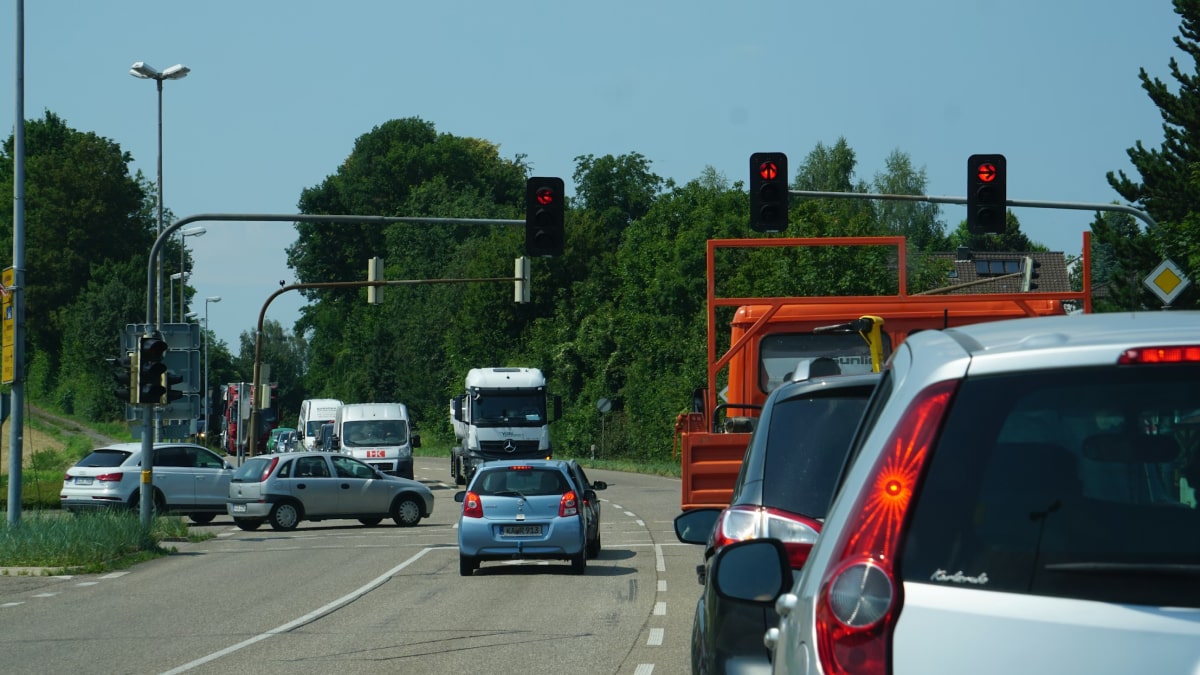 Motor vehicles queued at traffic lights on a wide urban road, highlighting car-centric street design.