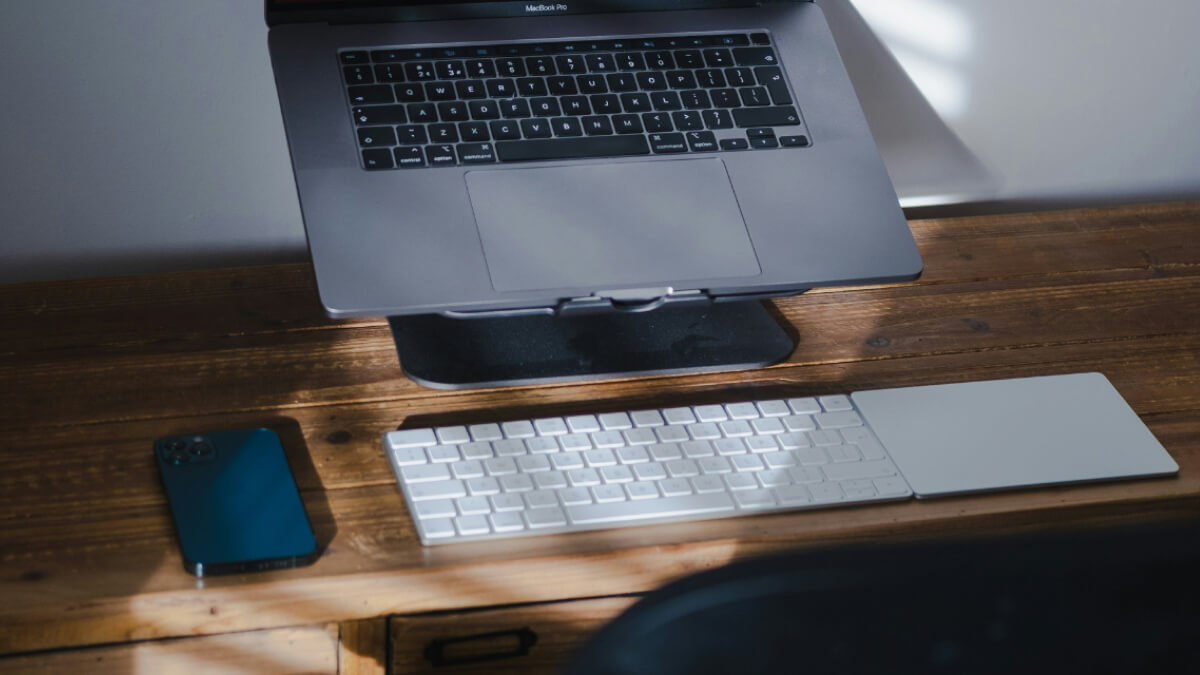 Work from home setup with laptop on stand, keyboard, trackpad and phone on desk.