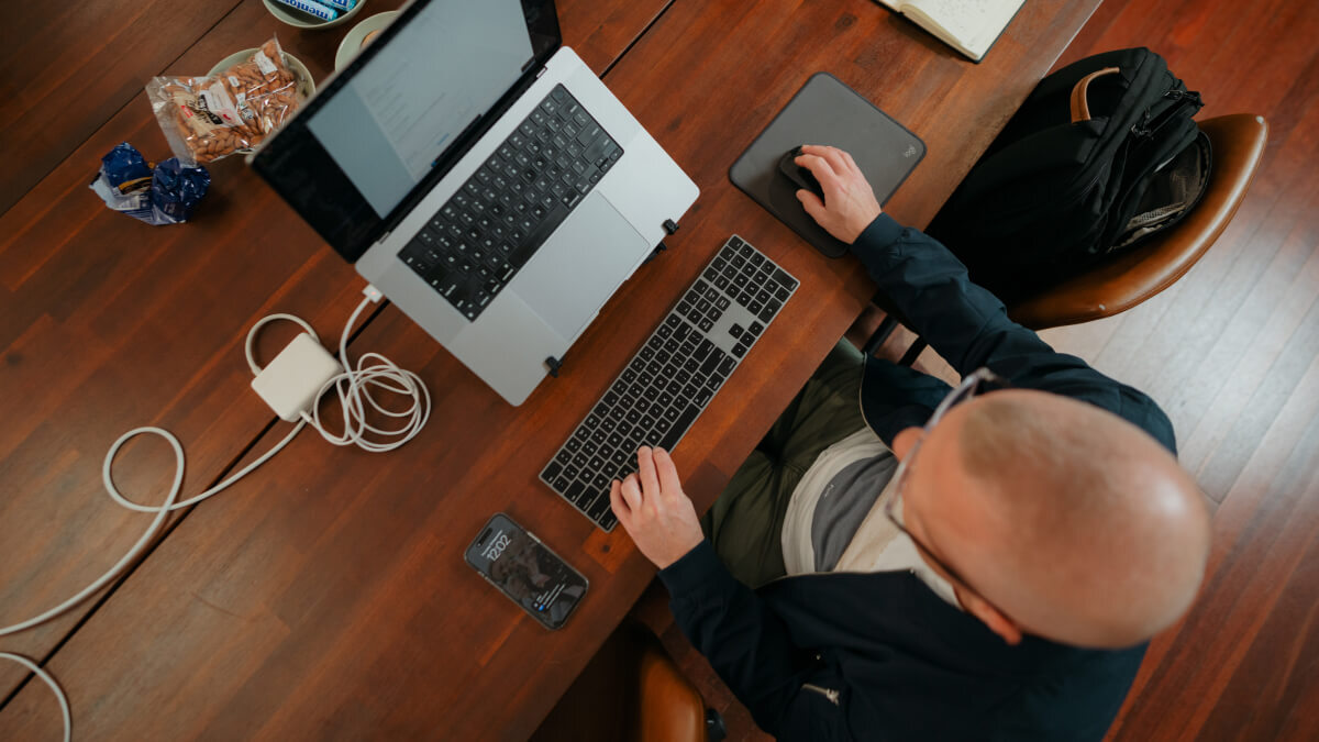 Overhead view of a software engineer working at a laptop, keyboard and mouse on a wooden desk.