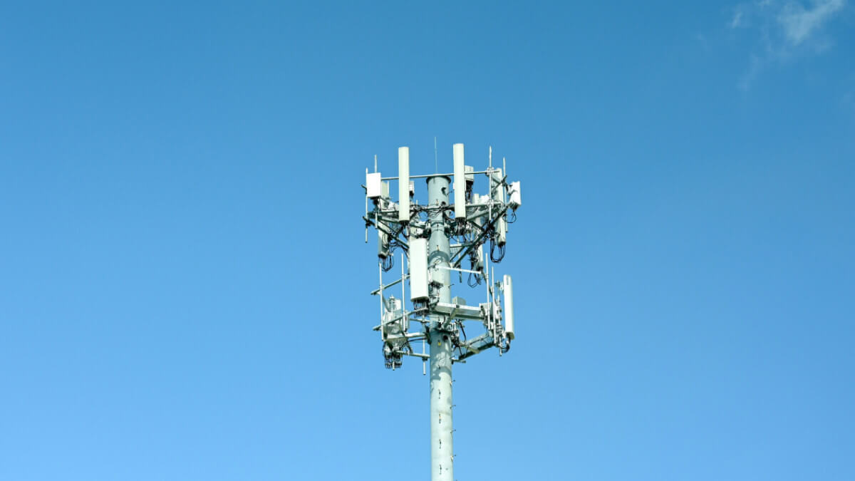 A mobile phone tower with multiple antennas against a clear blue sky.