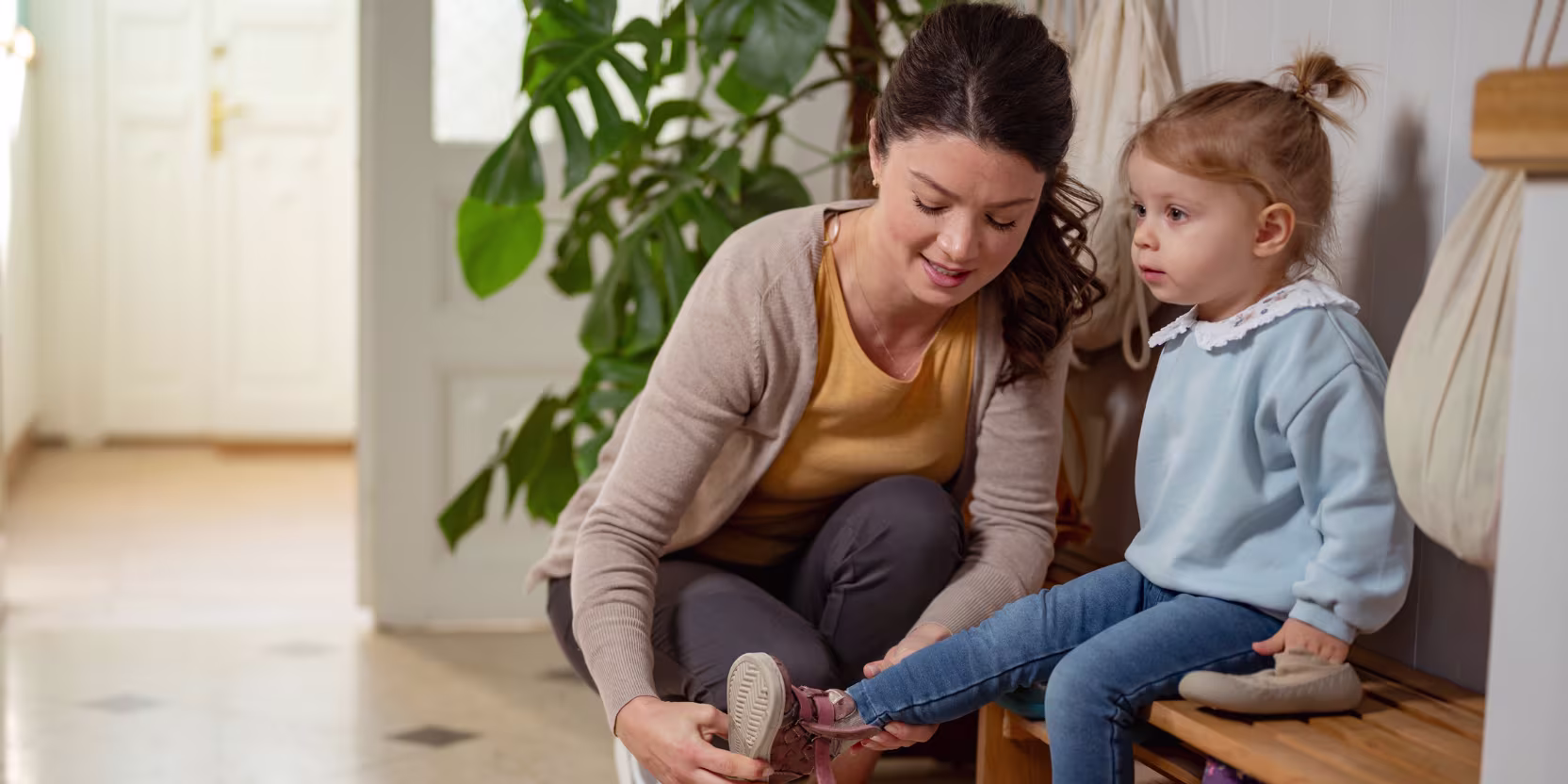 A young woman helps a little girl put on her shoes in a cozy home, showing care and support in a warm, nurturing environment
