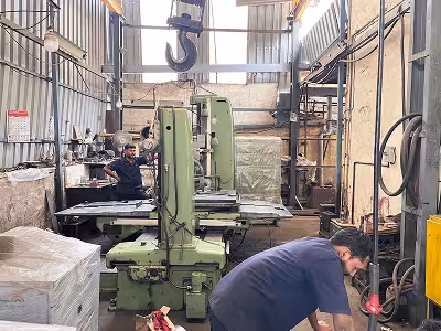 Two men working in an industrial workshop with large boring machine machinery and metal structures around.