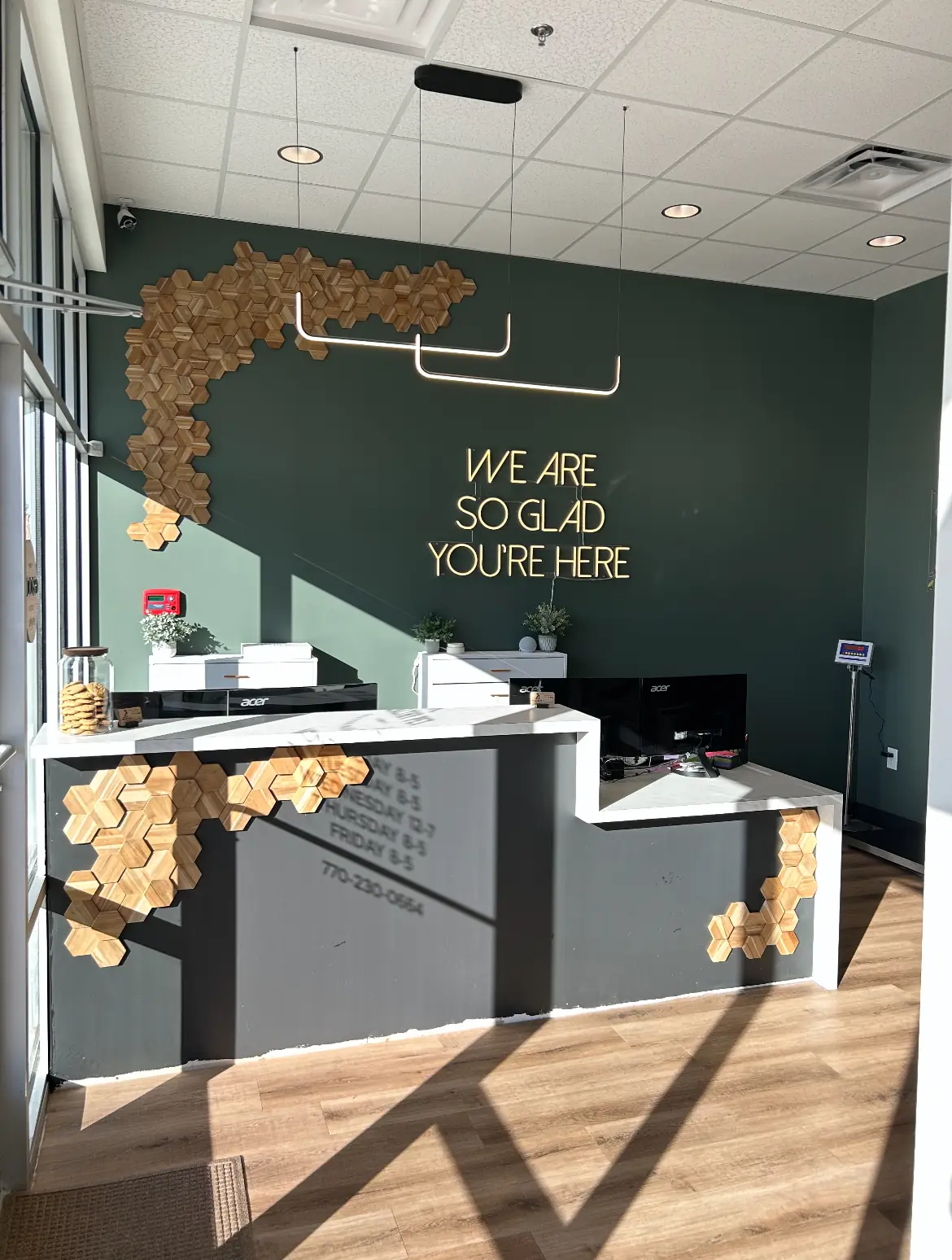 Reception desk with hexagonal wood decor and a wall sign reading We're so glad you're here.