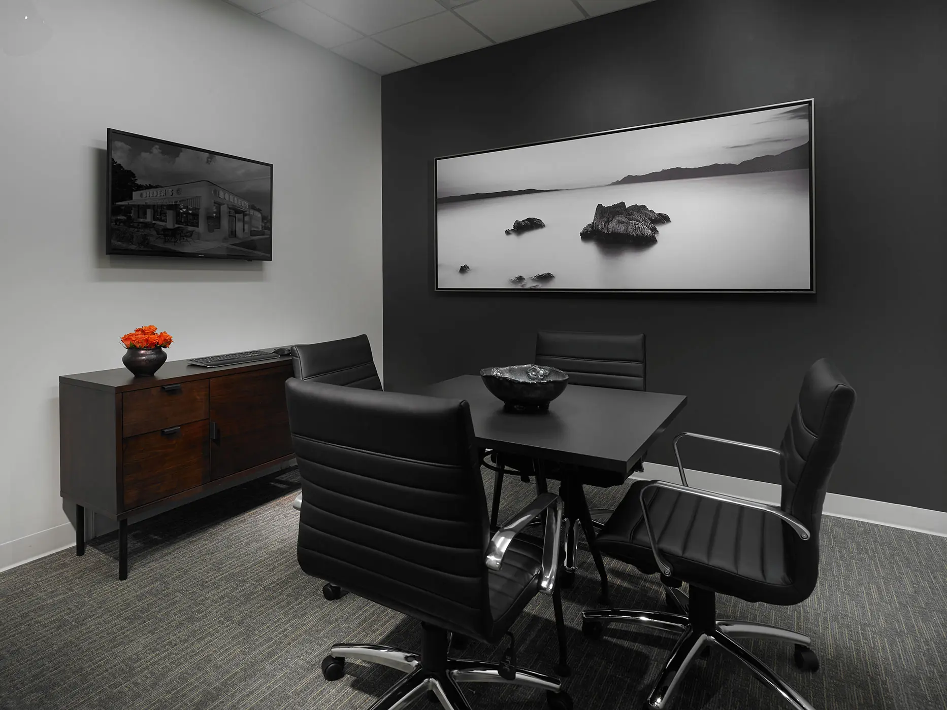 Modern office with a black table, four black chairs, a sideboard, and two wall-mounted black-and-white photos.