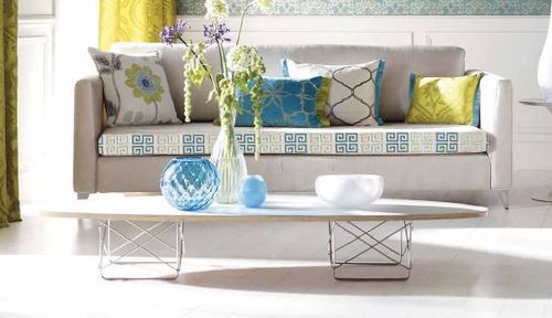 Modern living room with a gray sofa featuting Othello collection embroidery tapes (Ricamo) adorned with colorful geometric and floral pillows. Bright and inviting.