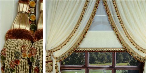 Elegant cream drapes with gold tiebacks and fringes of Larissa Collection frame a window, overlooking a lush garden. Decorative rope tiebacks add a touch of classic sophistication.