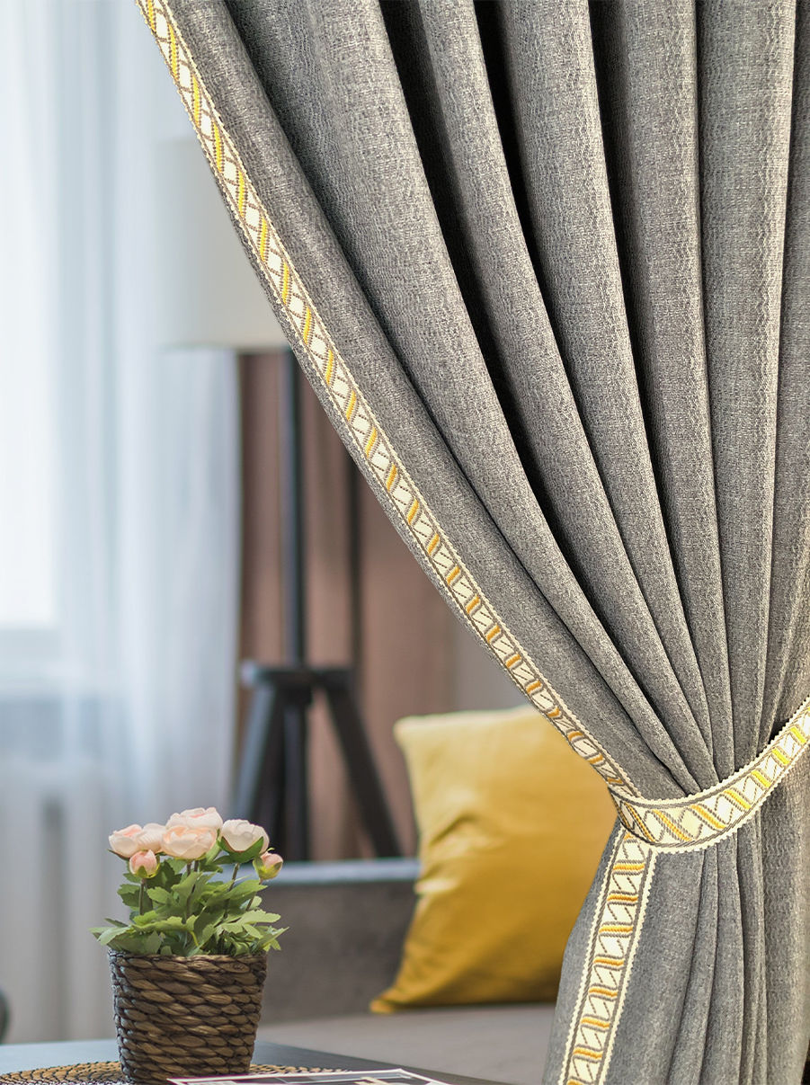 Gray curtain with yellow trims of our Aida Collection embroidery tapes reveals a cozy living room. A yellow pillow and potted flowers add warmth next to a softly lit window.