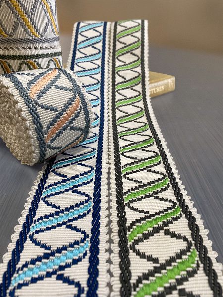Two rolls of decorative embroidery tapes, featuring geometric patterns in blue, green, and yellow, of Aida Collection on a table. The design is intricate and folk-inspired.