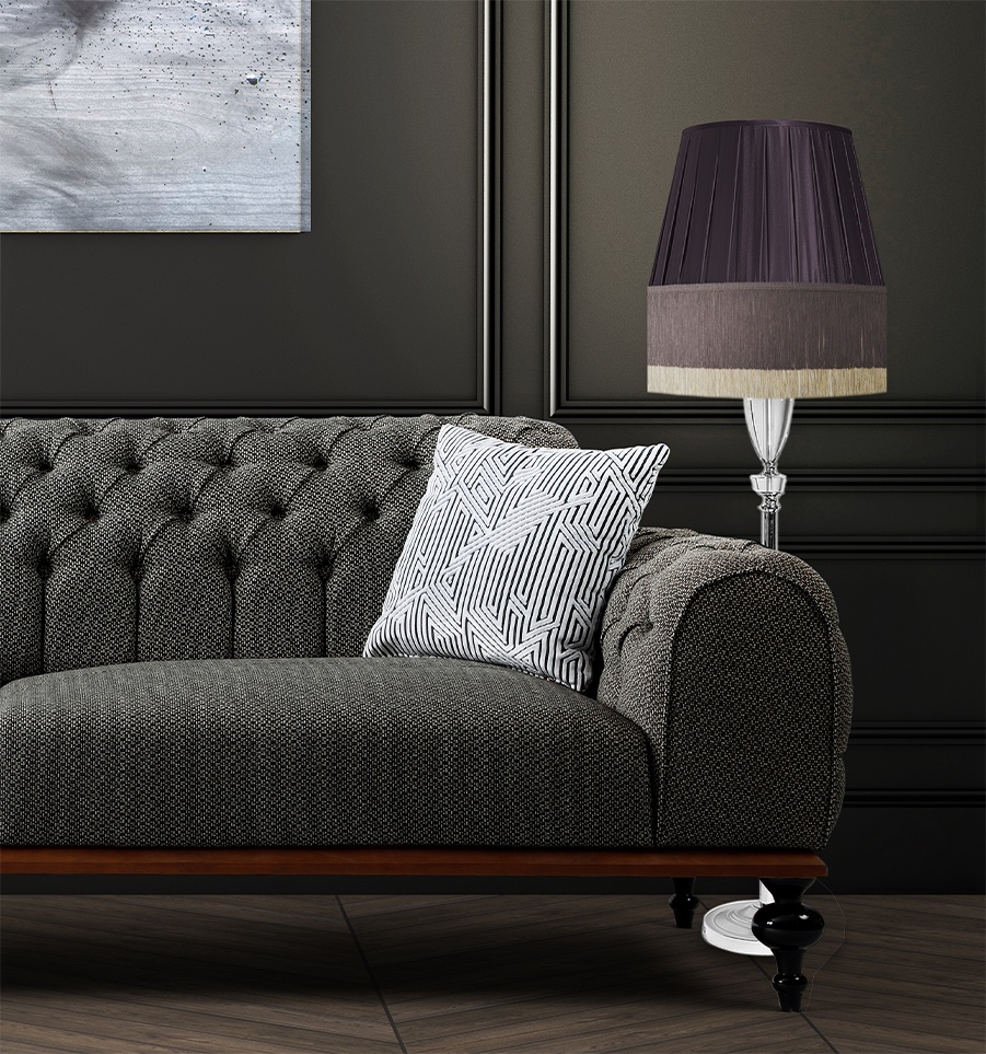 A chic, dark gray tufted sofa with a patterned pillow, beside a stylish lamp featuring our Doppio Nuovo Collection.