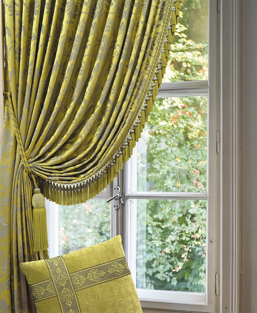 Elegant curtains drape over a window, featuring our Tsar Collection tiebacks and fringes, as well as braids on the matching pillow, creating a luxurious, serene atmosphere.