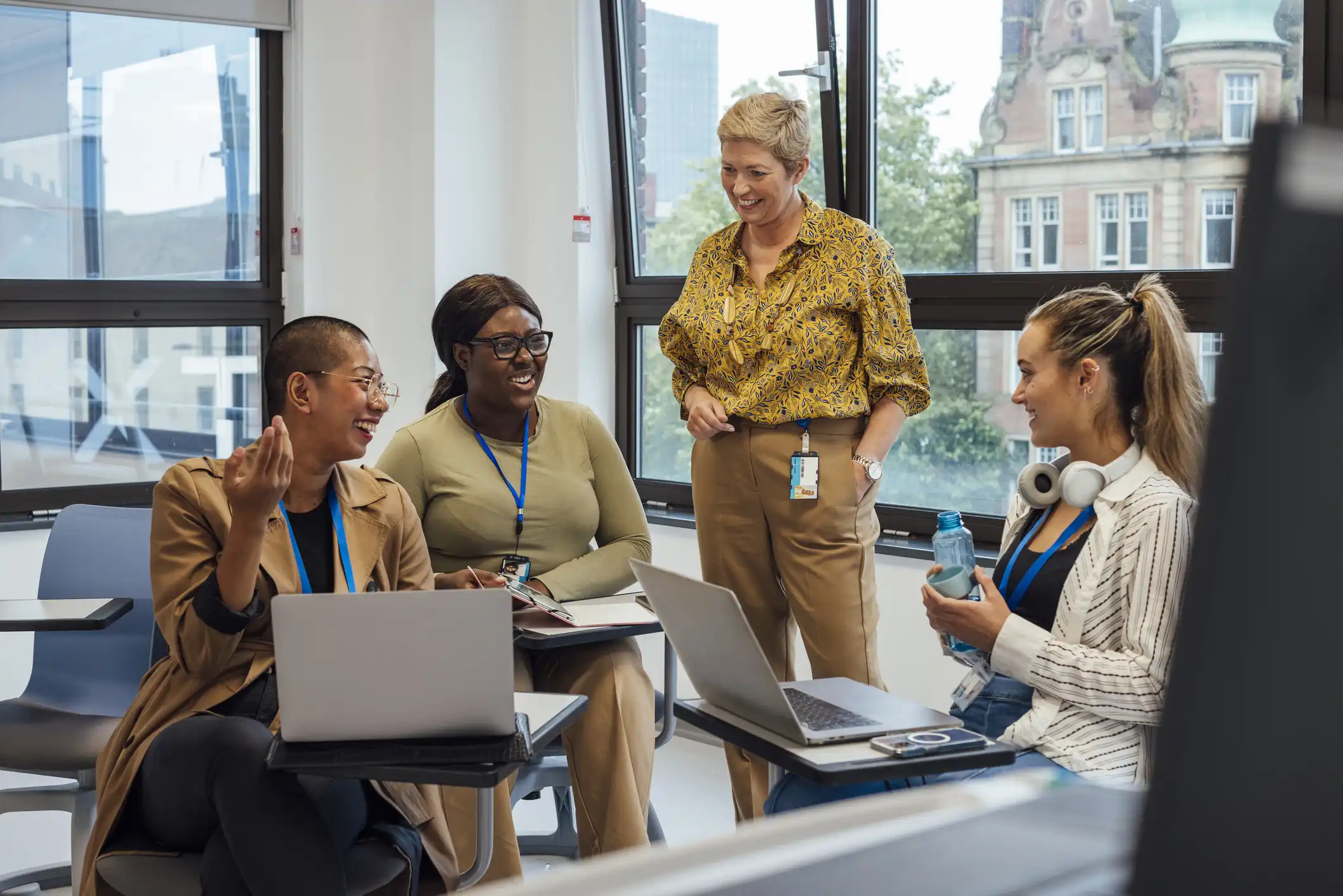 Teachers standing in a classroom talking and looking at computers.