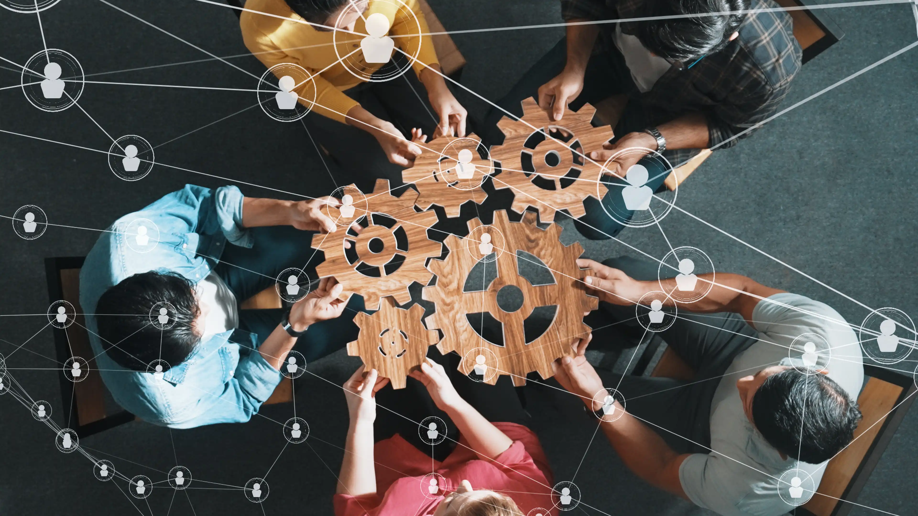 Top down view of five individuals sitting in a circle all holding onto interlocking wooden gears