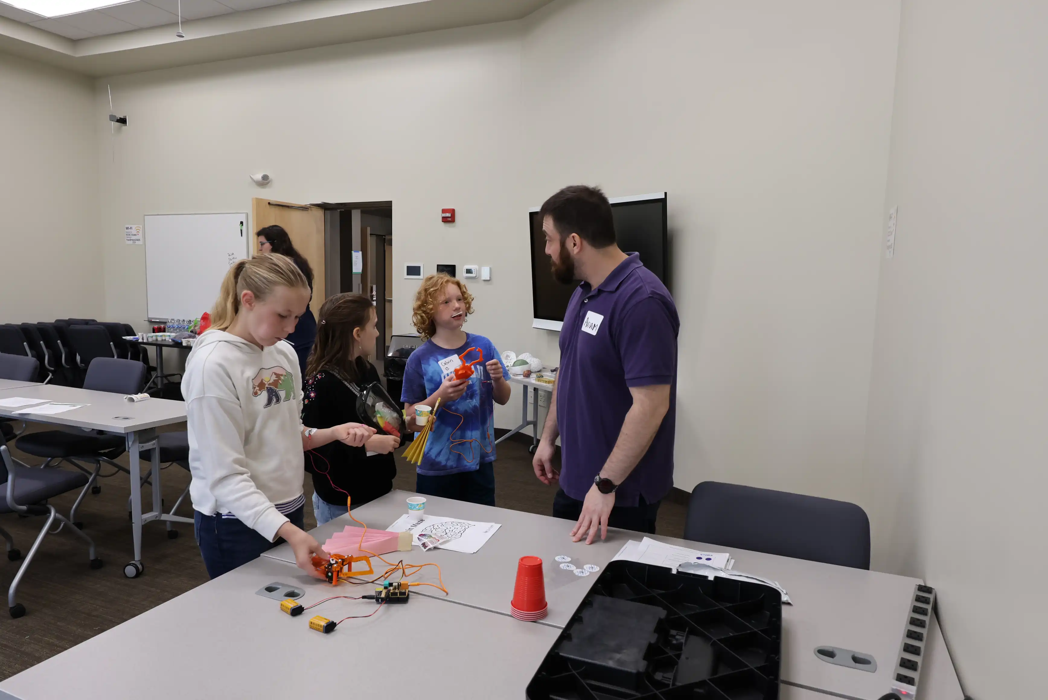 Students with adult by a table with cups and paper on it