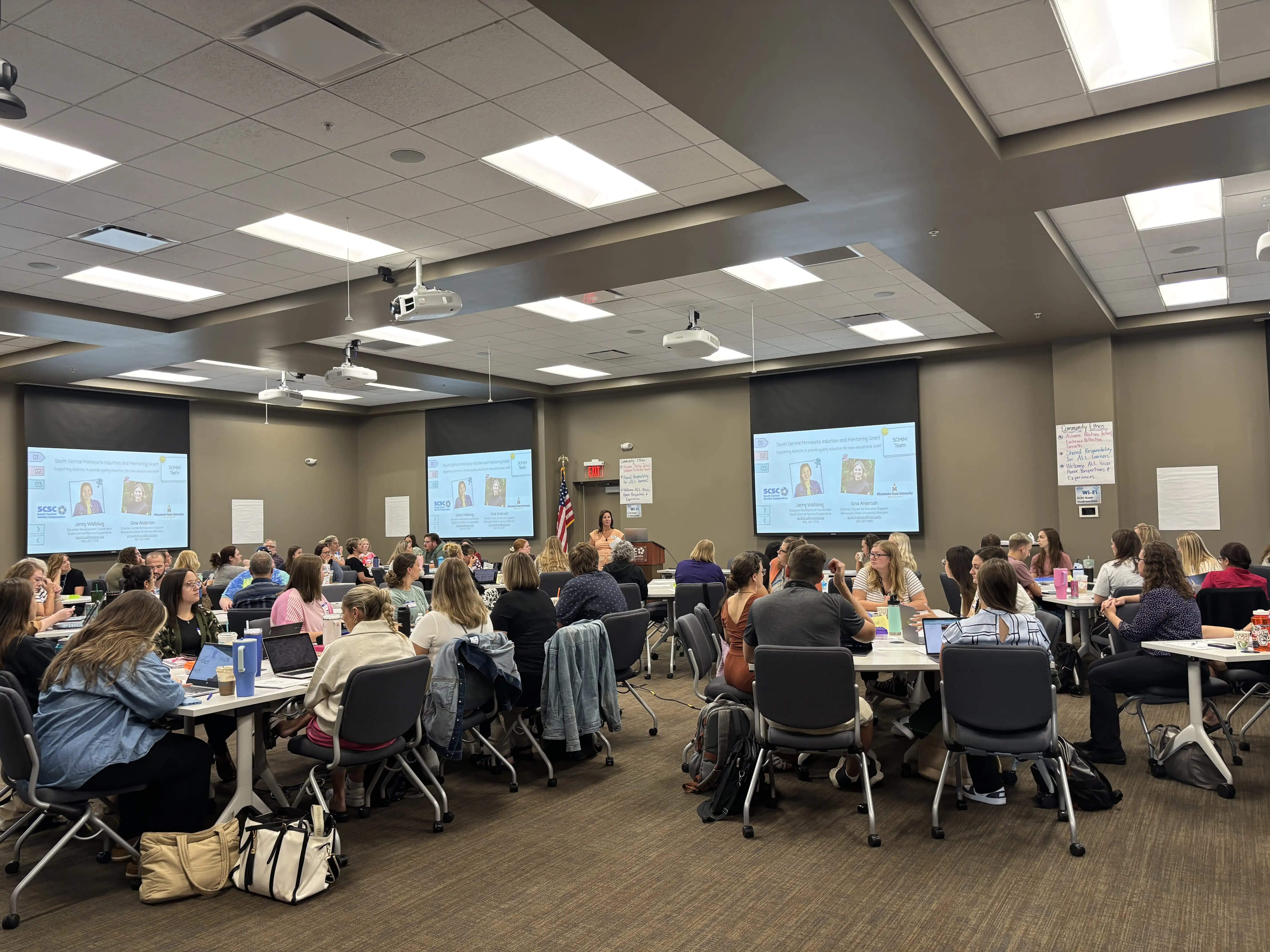 Attendees in a conference room at table pods listening to presentation