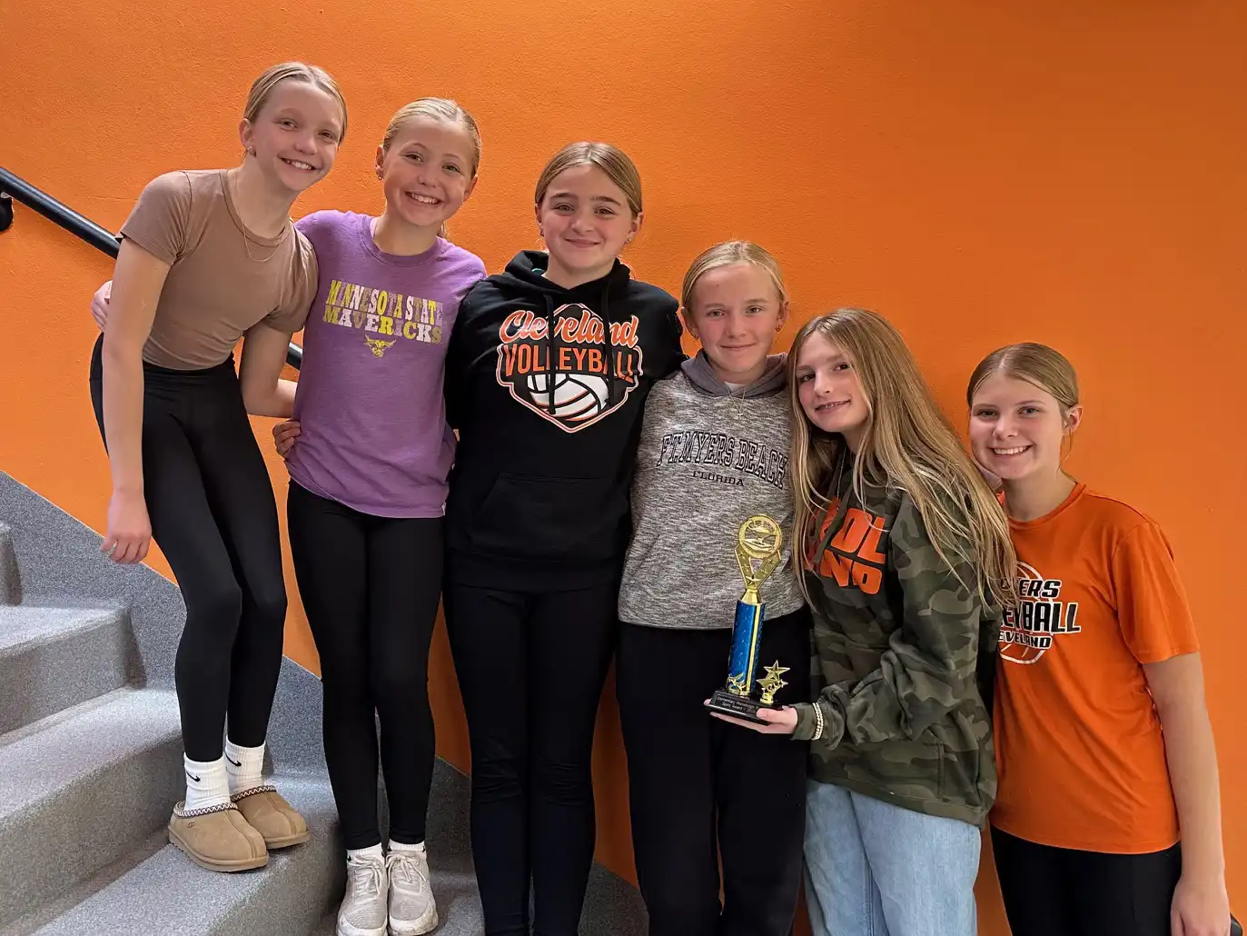 Students standing on stairs posing for a photo with their trophy