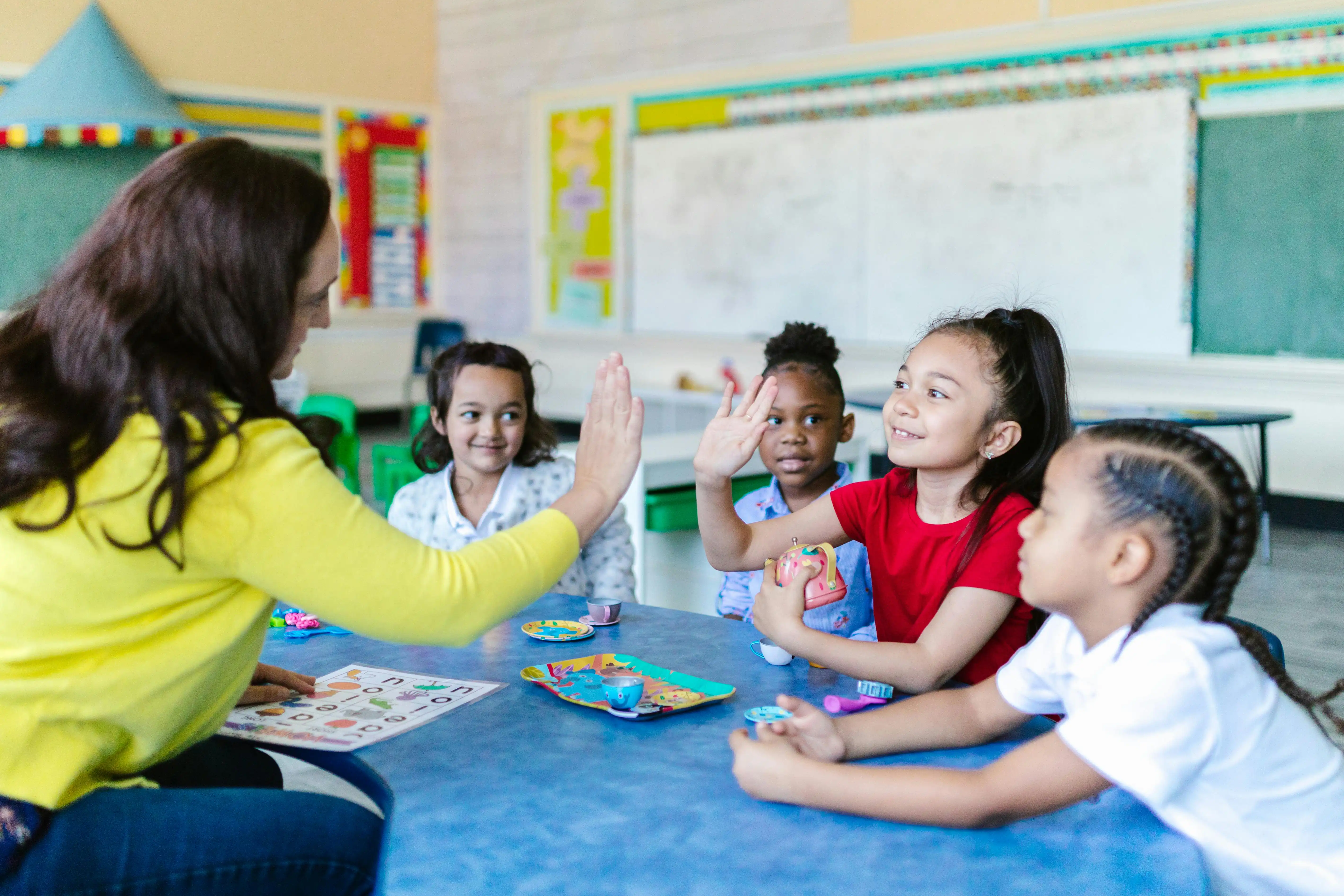 Adult with students sitting around a table learning letters of the alphabet