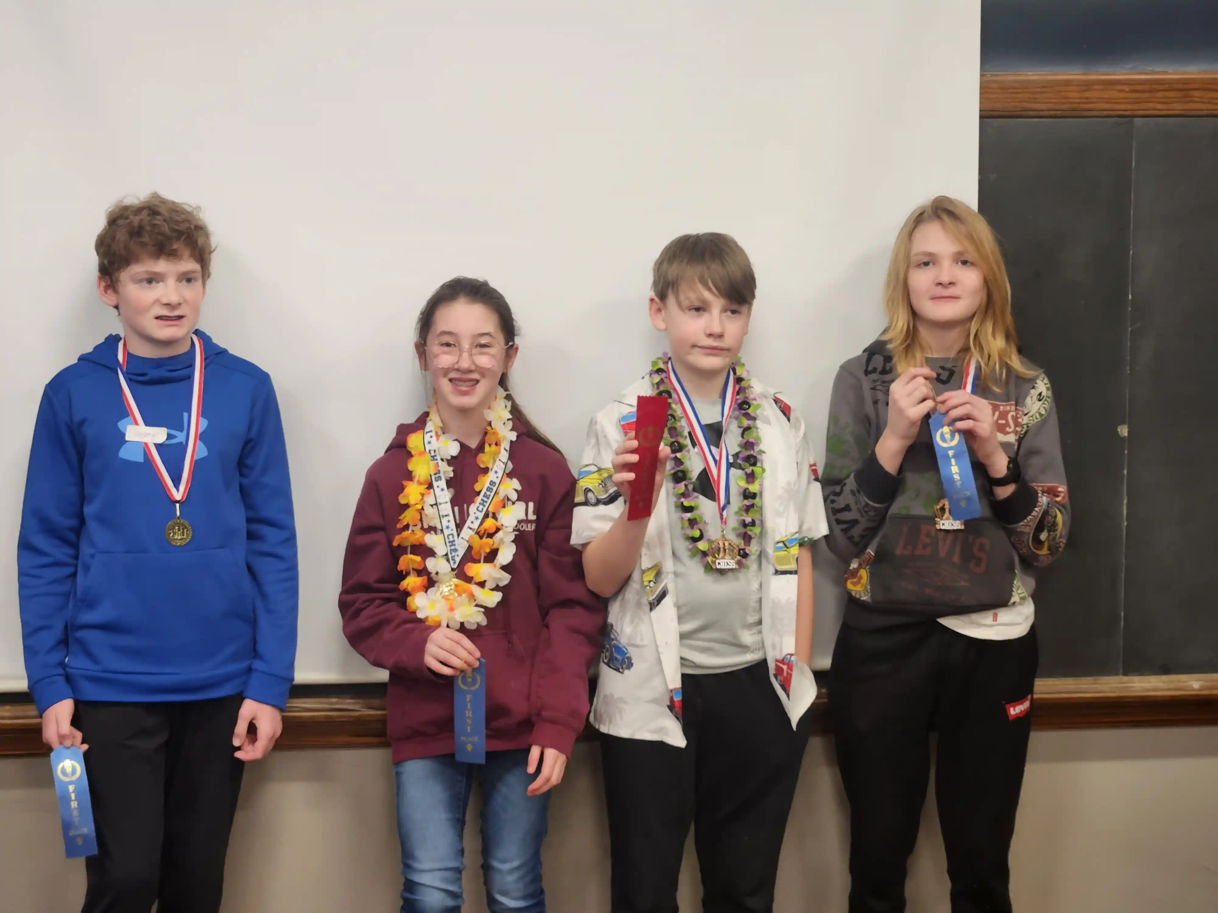 4 students smiling and facing the camera holding up their ribbons and wearing flowers around their necks.