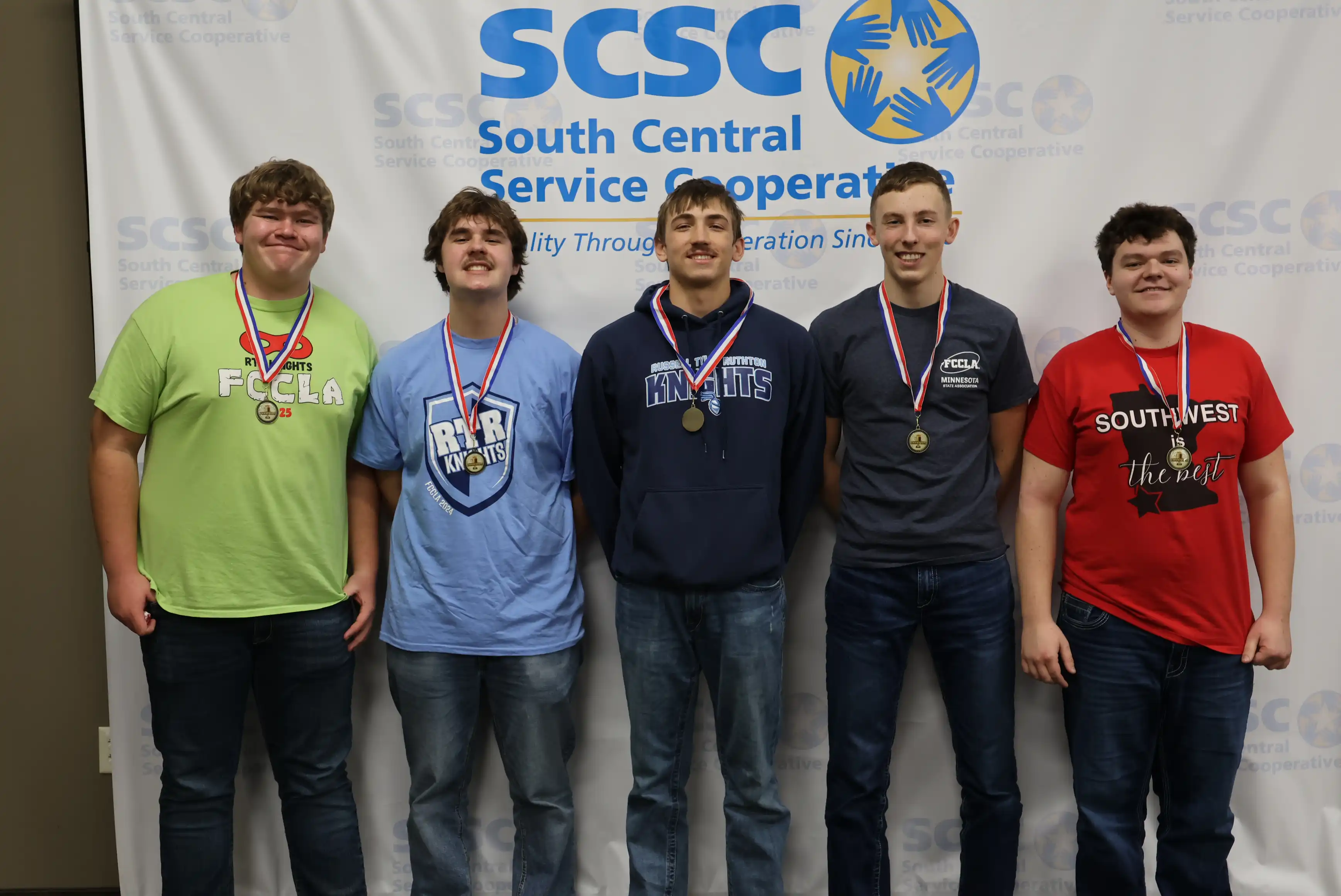 5 winner students standing in front of an SCSC sign wearing their medals