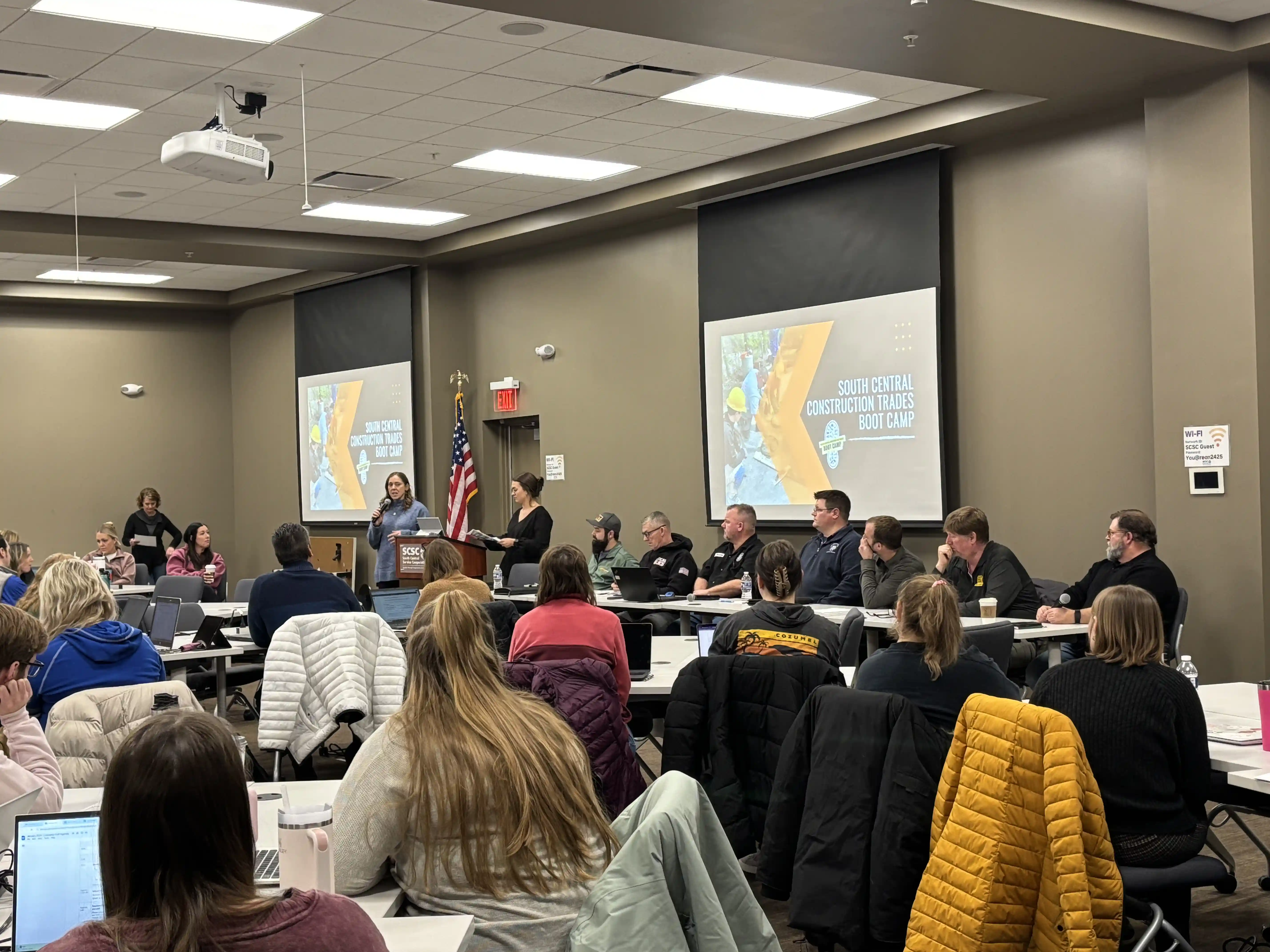Teachers sitting around tables listening to a panel talk about jobs in the trades industry.