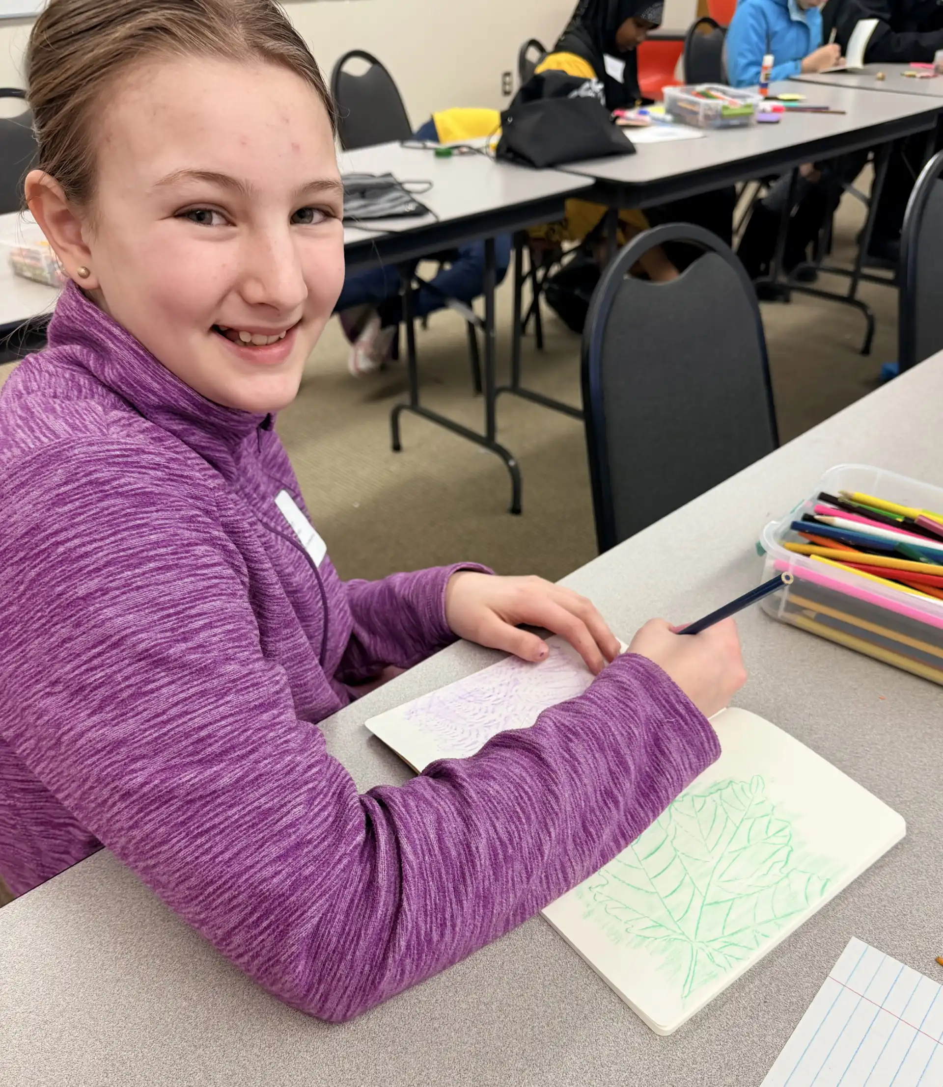 student smiling at the camera with her artwork on the table