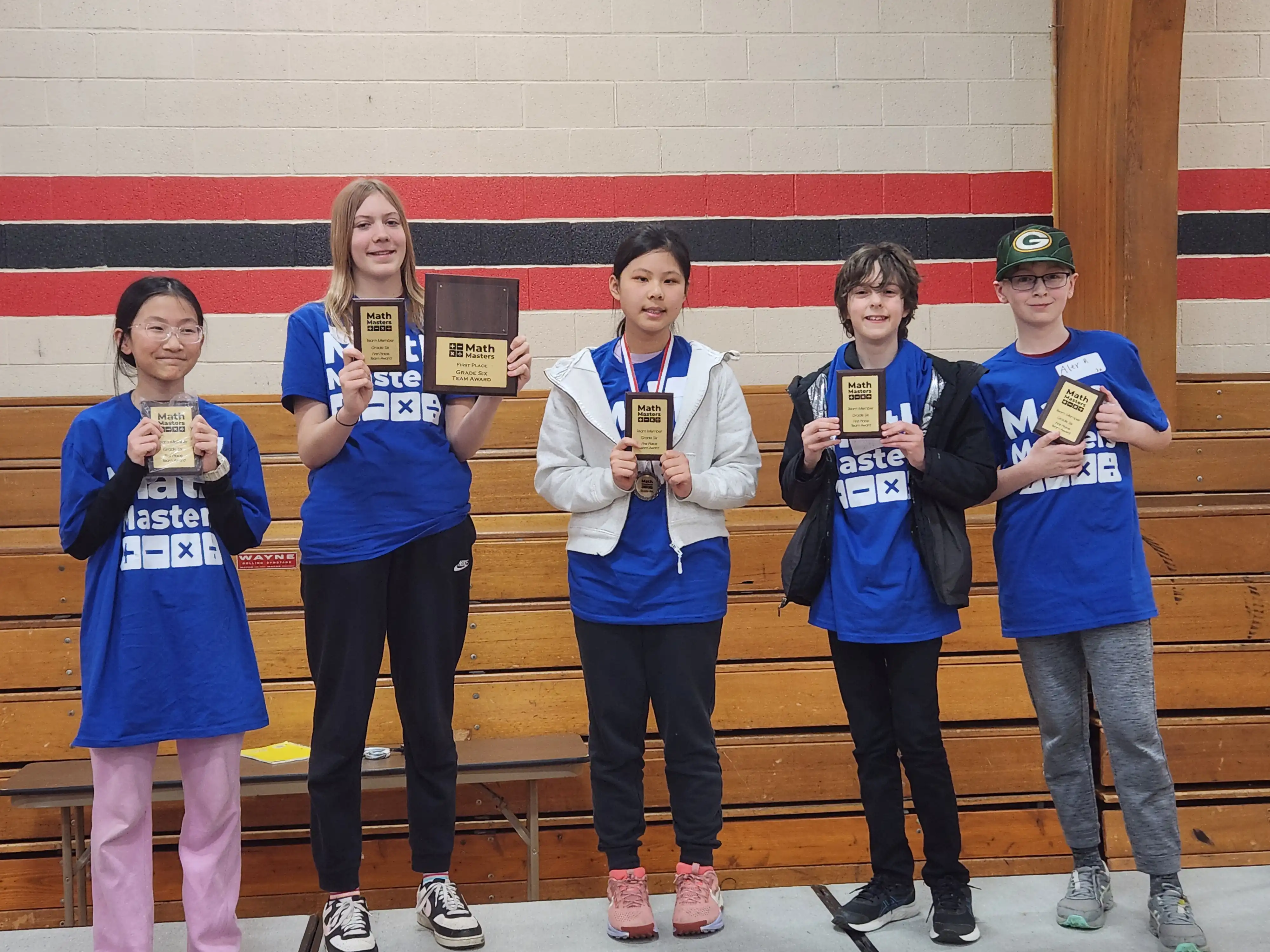 5 students standing on stage and smiling holding their award and wearing their medals.