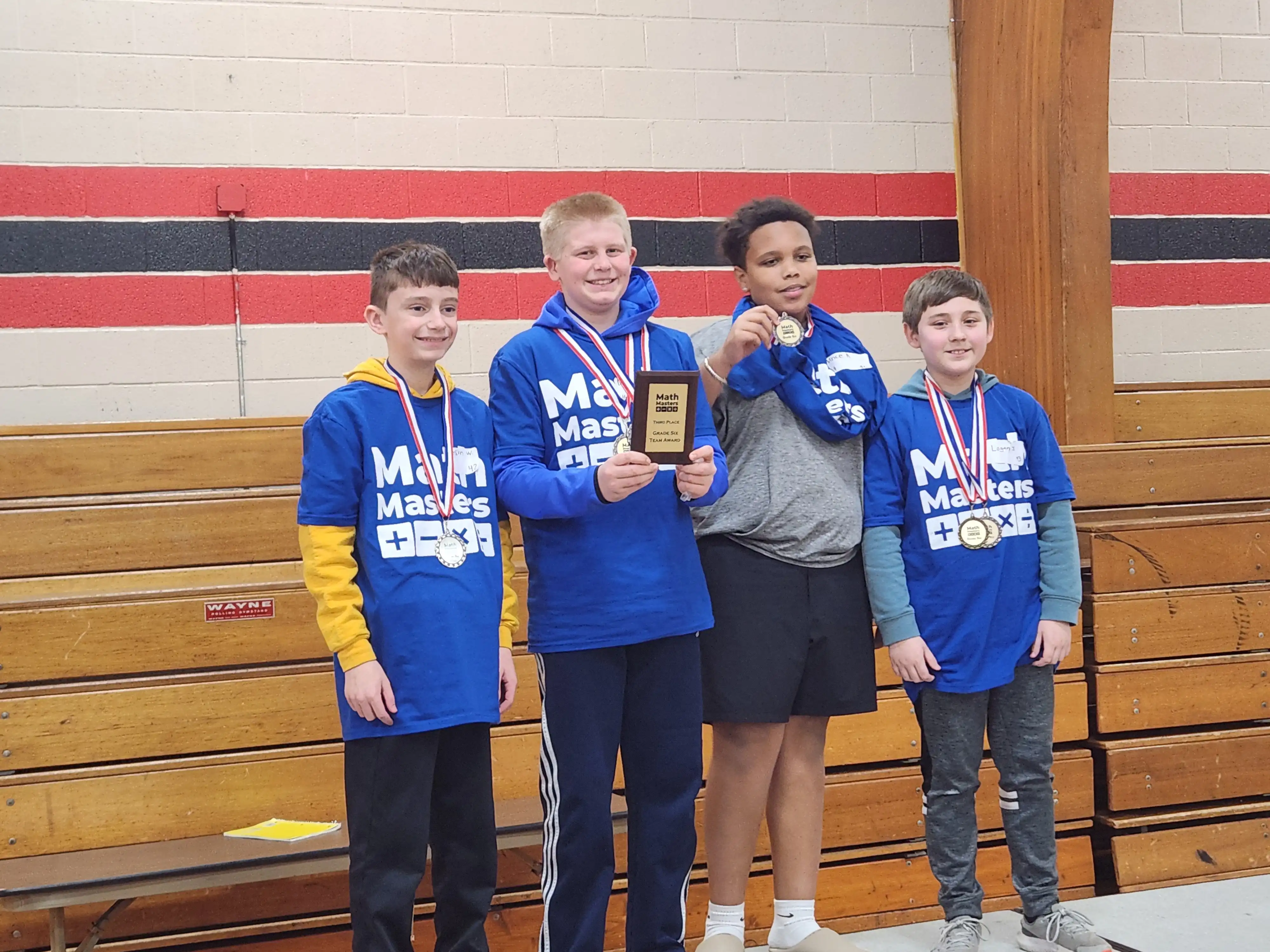 4 students smiling and standing on a stage holding their award and wearing their medals they earned
