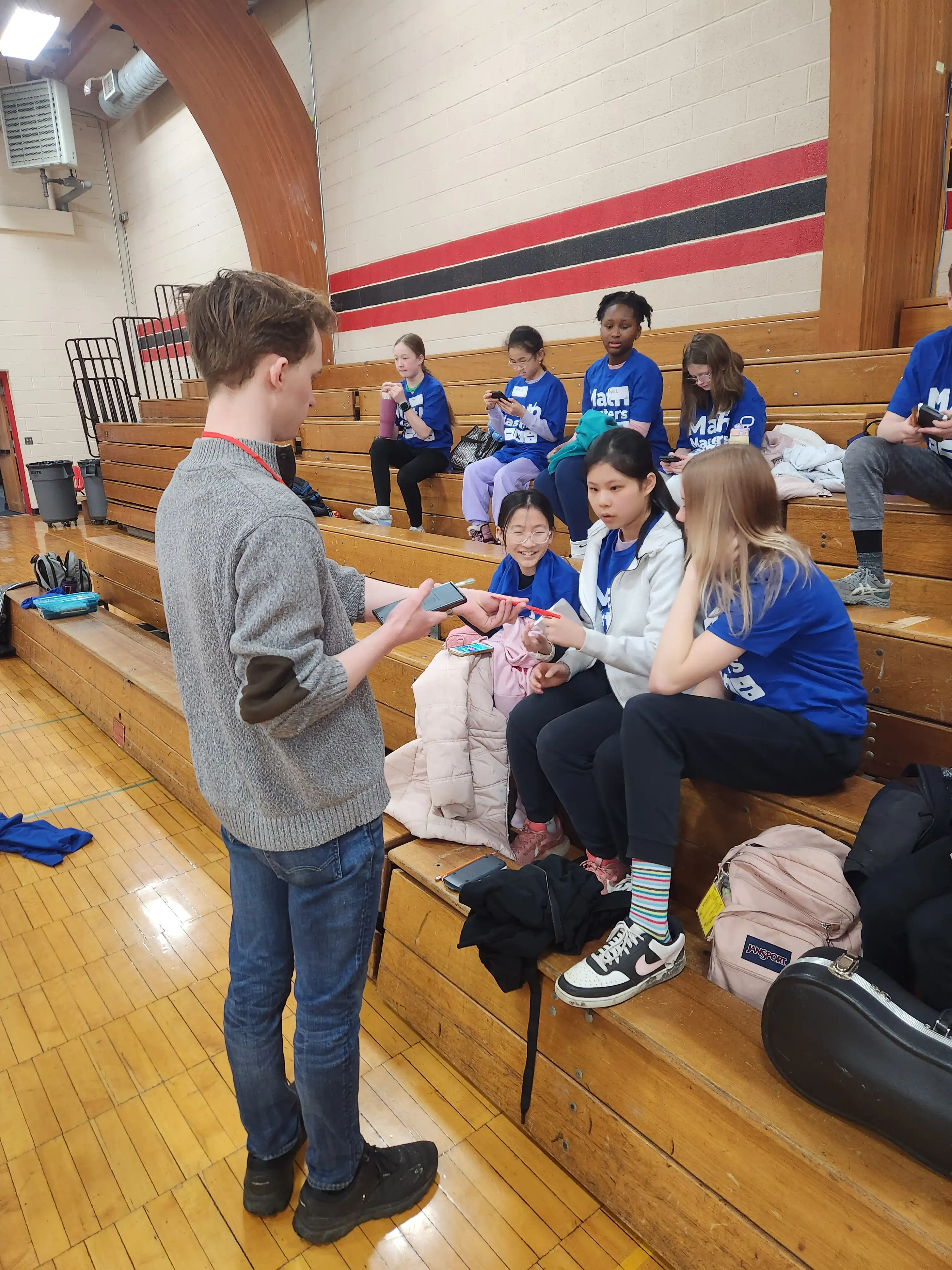 Leader of the event giving instructions to a group of students sitting on a bench.