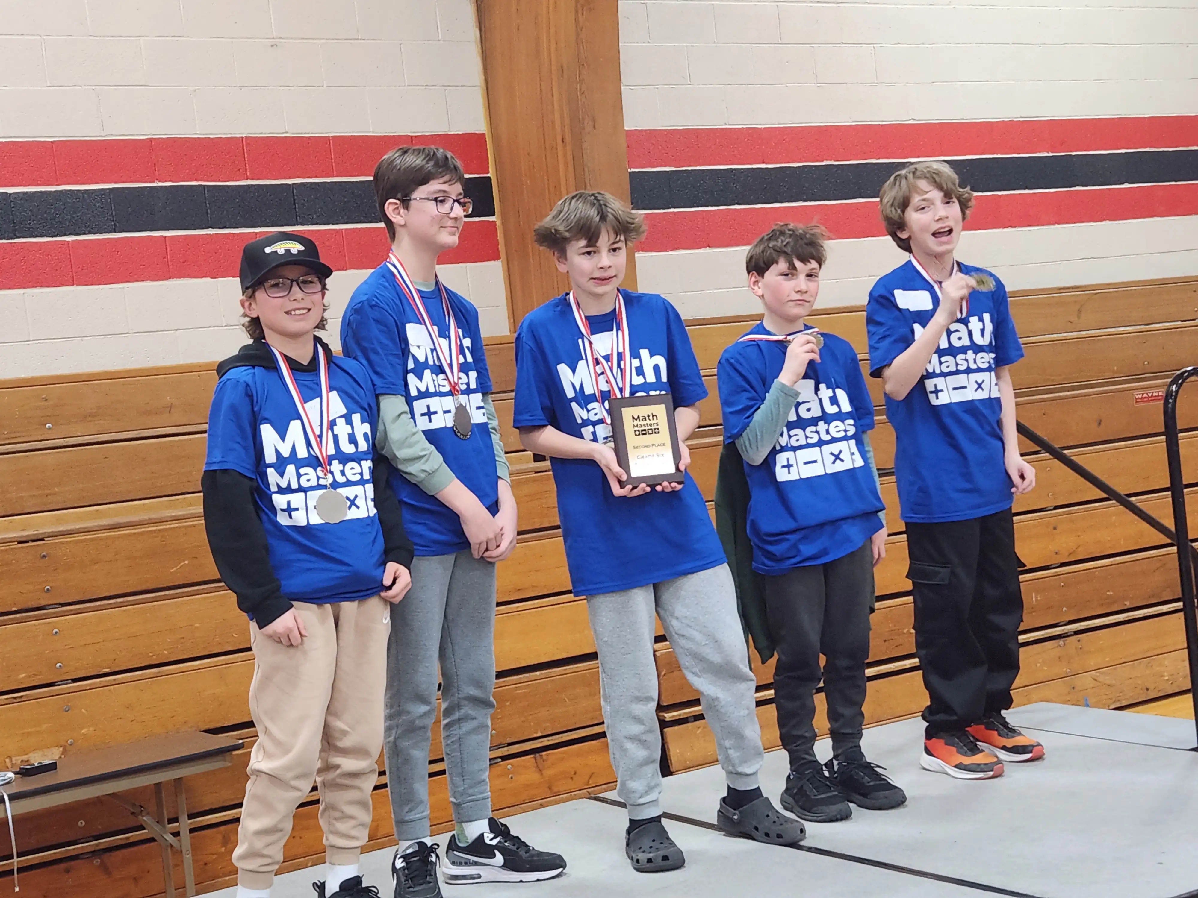5 students standing on stage and smiling holding their award and wearing their medals.