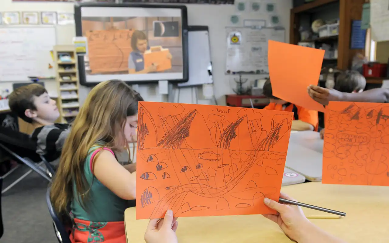 students holding up their drawings and showing the presenter on screen what they created.