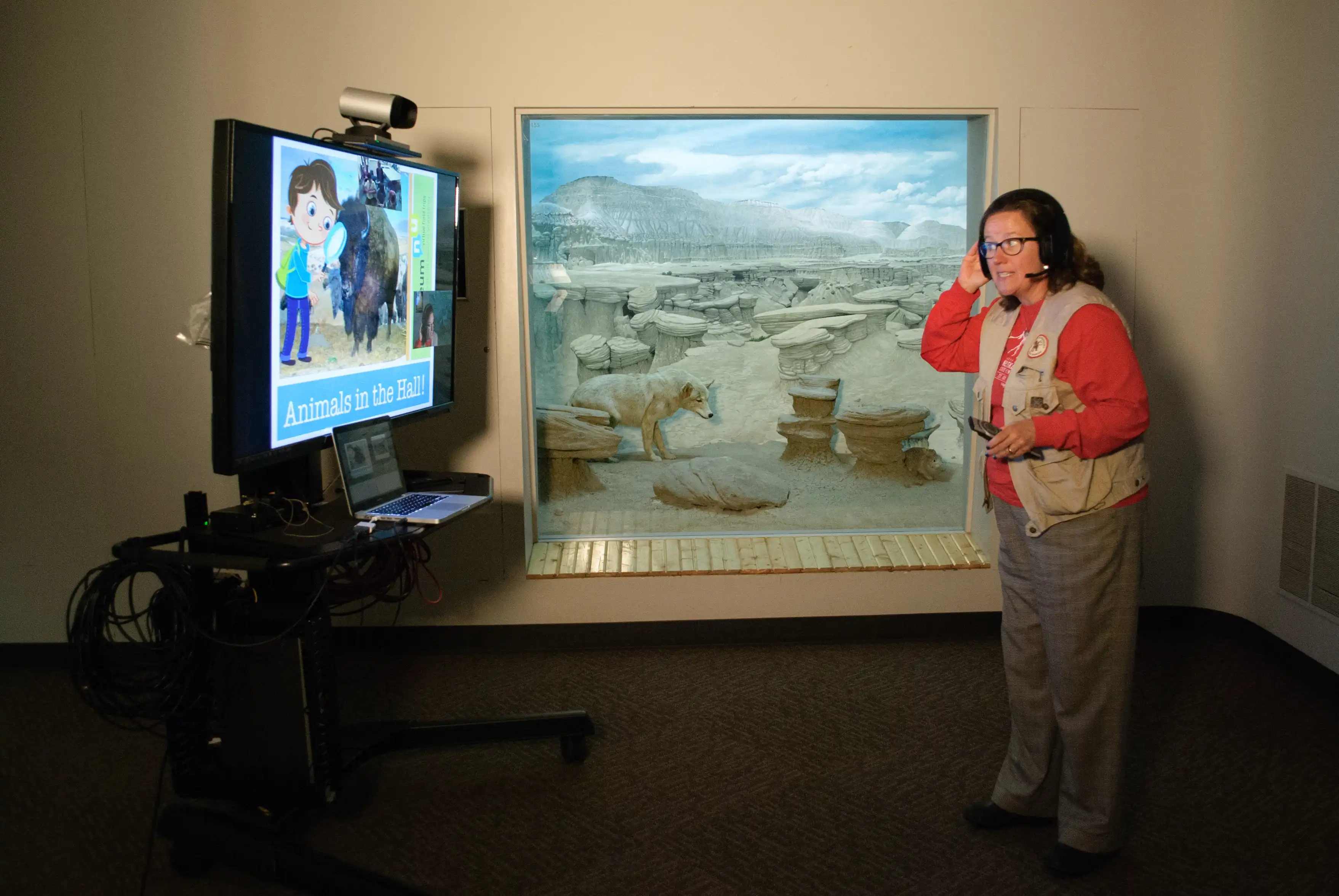 Presenter in a museum gallery presenting to students about the prairie wildlife ecosystem they are standing in front of.