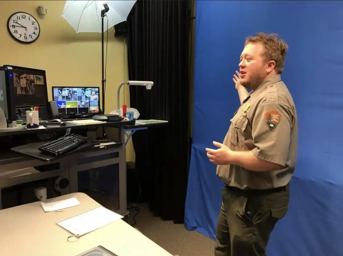 National Park Ranger presenting a program in a front of a blue screen to a group on the computer